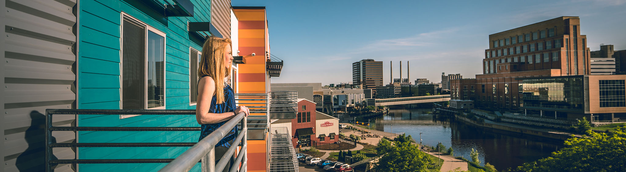 Woman standing on a balcony overlooking the Grand River and downtown Lansing